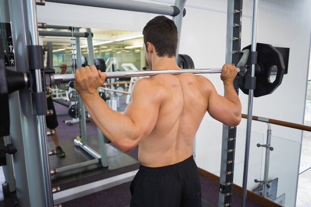 Shirtless muscular man lifting barbell in gym