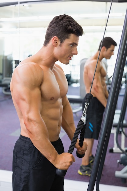 Shirtless muscular man using triceps pull down in gym