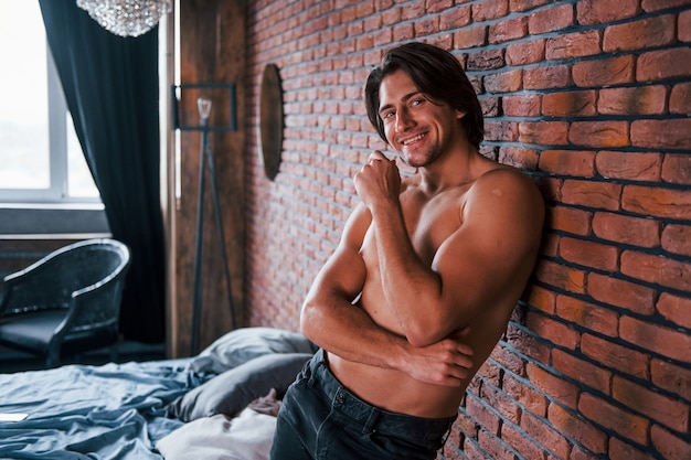 Shirtless sexy man leunend op de bakstenen muur in de slaapkamer op moment van de ochtend.