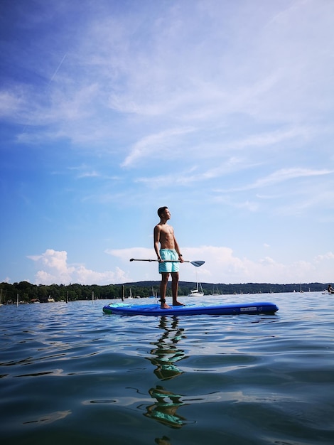 Shirtless tiener jongen paddleboarden in de zee tegen de lucht