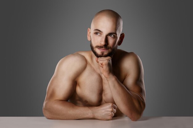 Shirtless turkish man think about idea leaning with elbow on\
table and having his fist on his chin