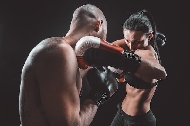 Shirtless vrouw trainen met trainer bij boksen en zelfverdediging les, studio, donkere ruimte