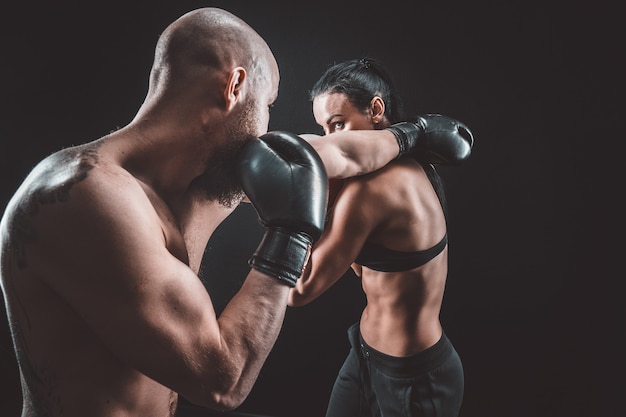 Shirtless vrouw trainen met trainer bij boksen en zelfverdediging les, studio, donkere ruimte