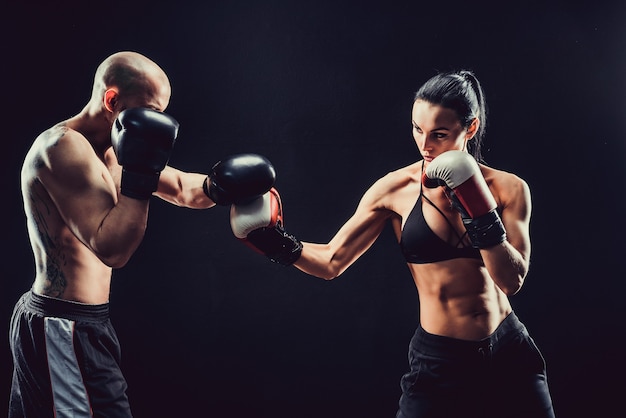 Shirtless vrouw trainen met trainer bij boksen en zelfverdediging les, studio, donkere ruimte
