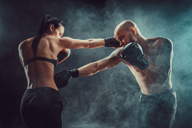 Photo shirtless woman exercising with trainer at boxing and self defense lesson, studio, dark background. female and male fight.