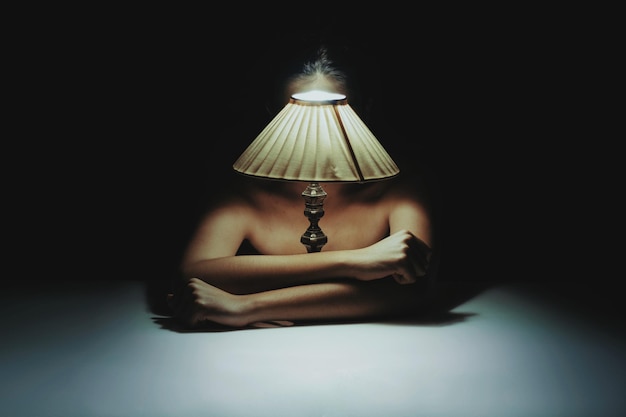 Photo shirtless woman sitting with illuminated lamp on table in darkroom