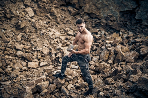 Shirtless young bodybuilder posing outdoor strong abs rock\
background front view