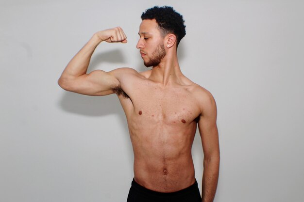 Photo shirtless young man flexing muscles against white background