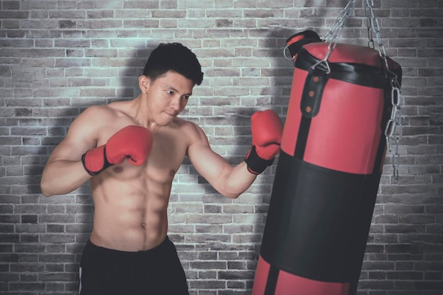 Shirtless young man hits on a boxing bag