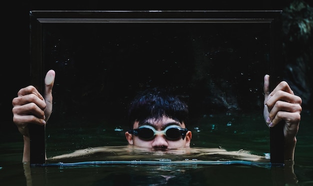 Photo shirtless young man holding frame while swimming in lake