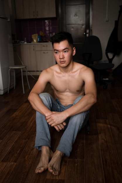 Photo shirtless young man sitting on hardwood floor