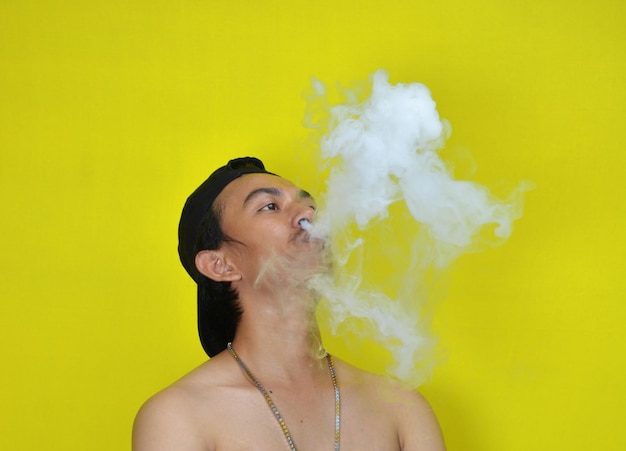 Shirtless young man smoking while standing by yellow background