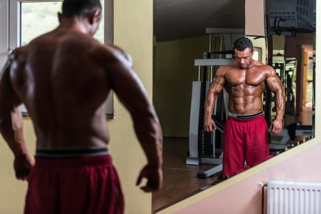 shirtloze bodybuilder die voor de spiegel poseert