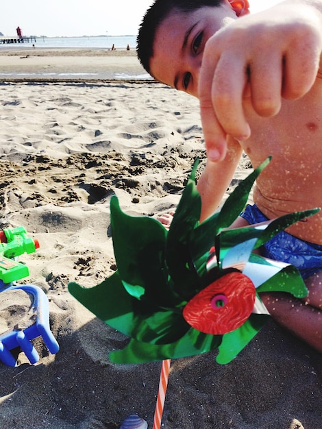 Foto shirtloze jongen die met een speelgoedwiel op het strand speelt