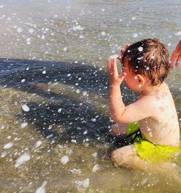 Shirtloze jongen spat water in de zee