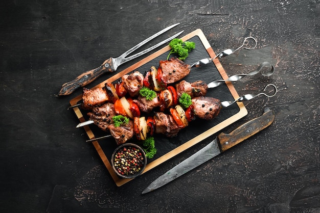 Shish kebab BBQ meat with onions and tomatoes On a black background Top view Free space for your text Rustic style