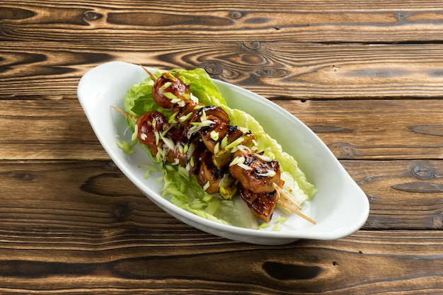 Шашлык из курицы и кабачков в соусе терияки с листьями салата и зеленым луком в красивой керамической тарелке на деревянном кухонном столе.