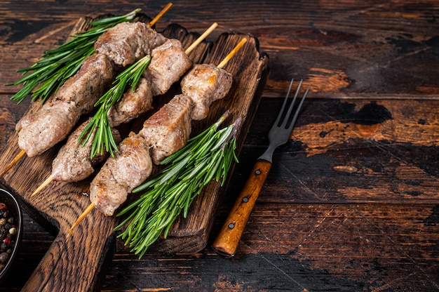 Shish kebab on skewers with herbs  on a wooden board. Dark wooden background. Top view. Copy space.