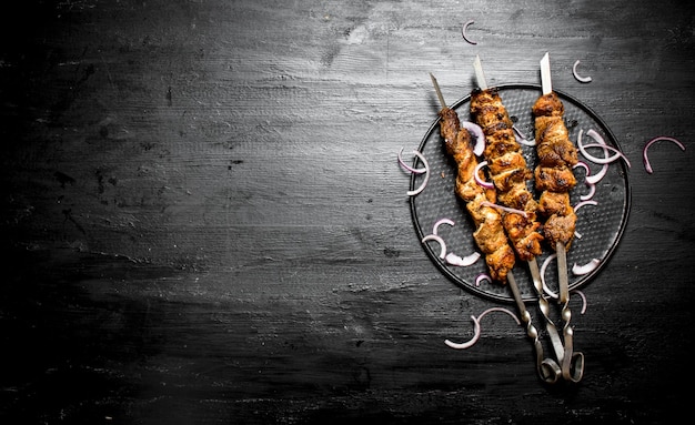 Shish kebab on skewers with onions. On the black wooden table.