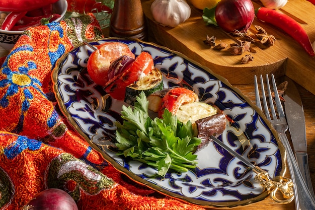 Shish Kebab of vegetables in a plate with a traditional Uzbek ornament. Eggplant, zucchini, tomatoes and onions fried on a skewer.