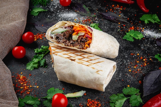 Shoarma burrito gesneden met groenten en kruiden op een donkere stenen tafel Het concept van fastfoodrestaurants