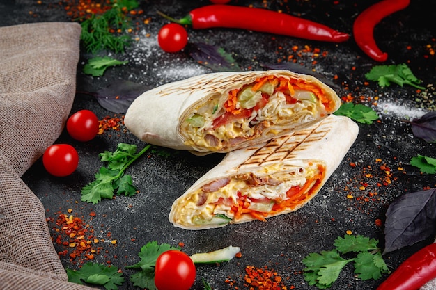 Shoarma burrito gesneden met groenten en kruiden op een donkere stenen tafel het concept van fastfoodrestaurants