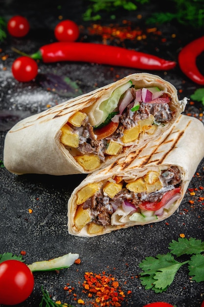 Shoarma burrito gesneden met groenten en kruiden op een donkere stenen tafel Het concept van fastfoodrestaurants