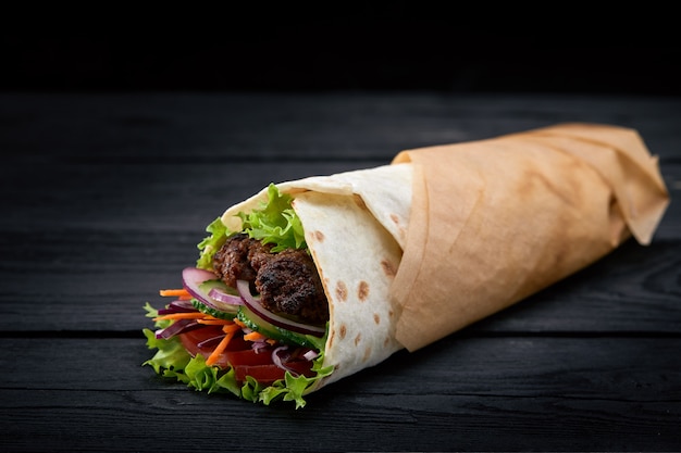 Shoarma gerold in lavash, vochtig gegrild vlees met ui, kruiden en groenten op houten zwarte achtergrond.