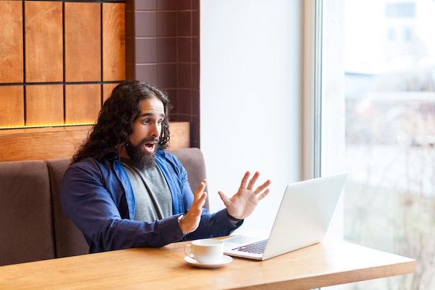 Shoched knappe jonge volwassen man freelancer in casual stijl zittend in café en sla wijzigingen van het rapport niet op in laptop, hand tonend aan notebook zoals stoppen met werken. Binnen, levensstijlconcept