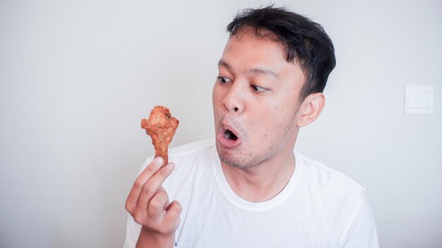 若いアジア人男性の衝撃とすごい顔はフライドチキンを着て白いシャツを食べています