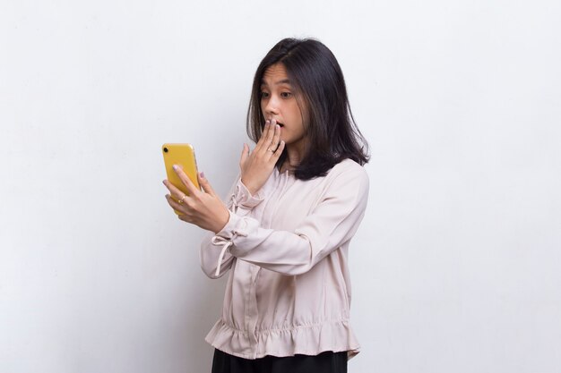 Shock giovane bella donna asiatica utilizzando il telefono cellulare isolato su sfondo bianco