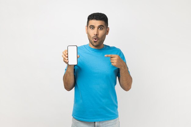 Shocked amazed man pointing at smart phone with blank white display mockup for promotional text