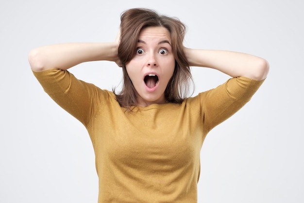 Shocked amazed young woman with hands on head standing and shouting