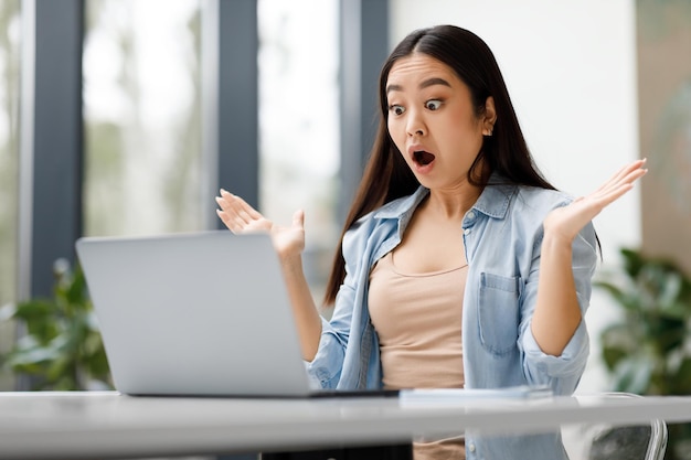 Shocked asian female student using laptop computer receive good news message looking at screen with