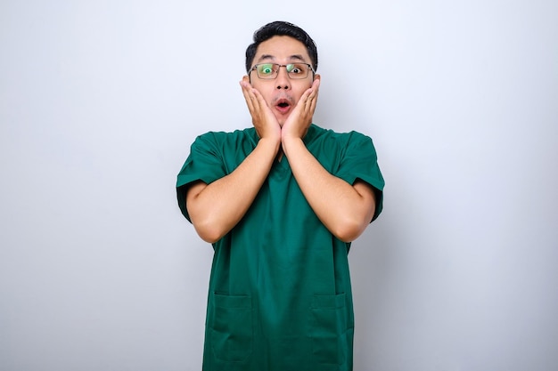 Shocked asian male nurse doctor in scrubs hear horrible news gasping cover mouth with hands and stare at camera