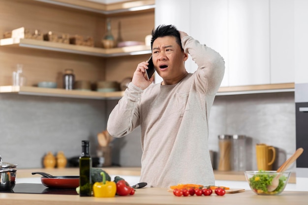 식사를 요리하고 전화 통화를 하는 충격을 받은 아시아 남자