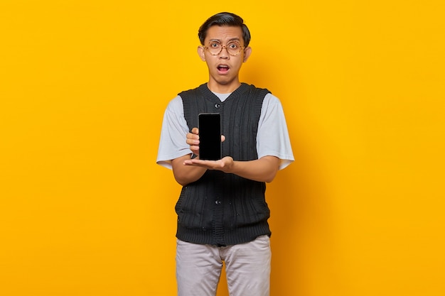 Shocked Asian man showing blank smartphone screen with palm. product promotion concept