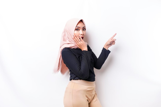 Shocked Asian Muslim woman pointing at the copy space on beside her isolated by white background