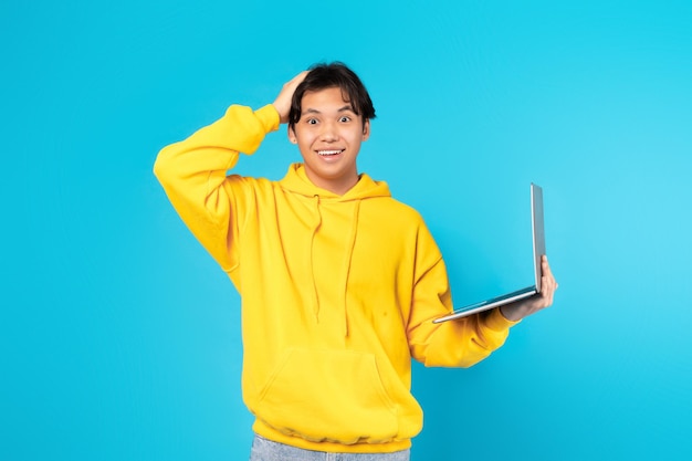 Shocked Asian Teen Boy Holding Laptop Touching Head Studio Shot