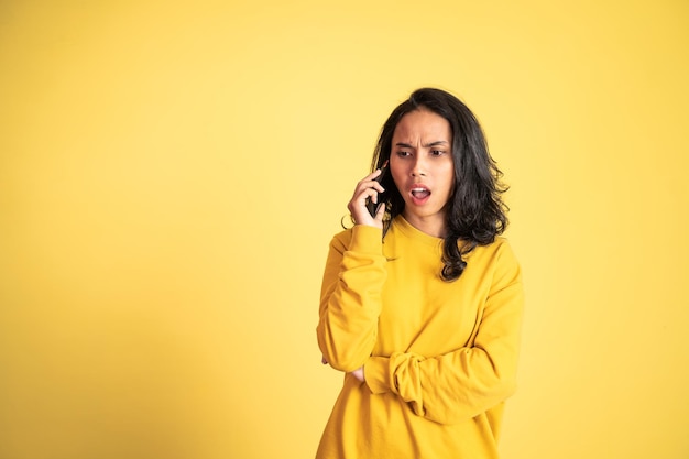 Photo shocked asian woman making a call using a cell phone on isolated background