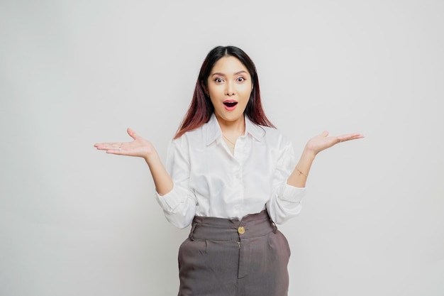 Shocked Asian woman wearing white shirt pointing at the copy space beside her isolated by white background