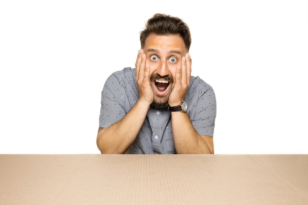 Shocked and astonished man opening the biggest postal package. Excited young male model on top of cardboard box looking inside. 