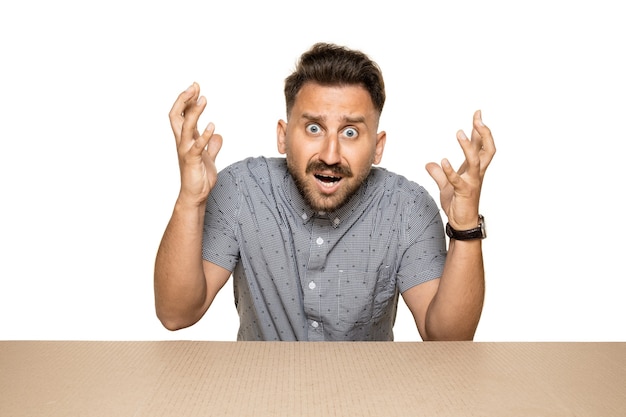 Shocked and astonished man opening the biggest postal package. Excited young male model on top of cardboard box looking inside.