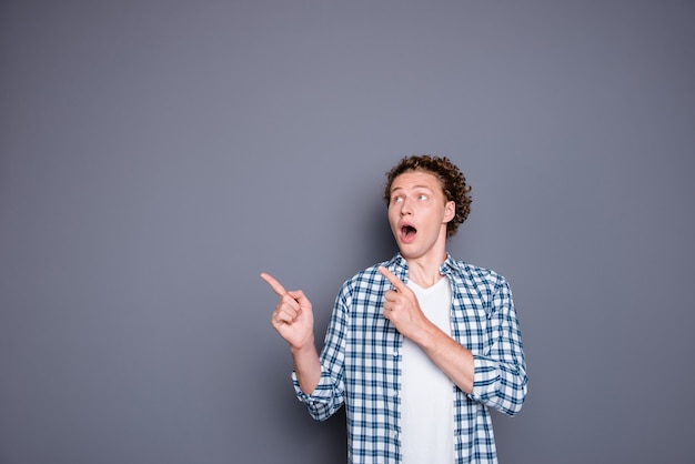 Shocked attractive young guy in casual checkered shirt pointing two fingers aside