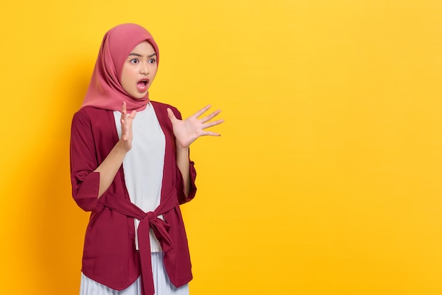 Shocked beautiful Asian woman in casual shirt looking at copy space with amazed face isolated over yellow background