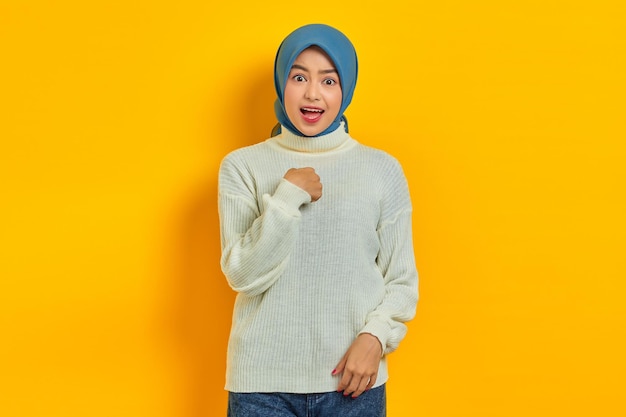 Shocked beautiful Asian woman in white sweater n hijba pointing fingers at herself isolated over yellow background