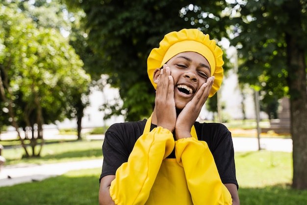 Scioccato adolescente africano nero cuoco con cappello da chef e grembiule giallo uniforme tenere le guance e sorpresa pubblicità creativa per bar o ristorante