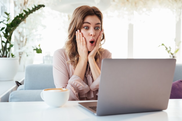 Shocked blondy woman in blouse sitting by the table