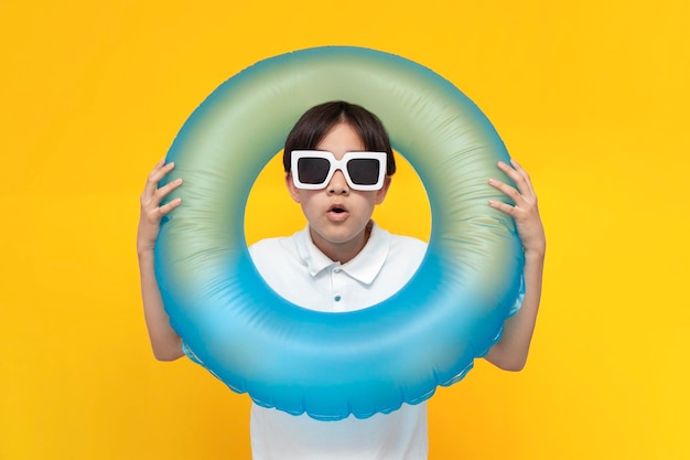 Шокированный мальчик-подросток двенадцати лет в солнцезащитных очках с надувным кольцом для плавания