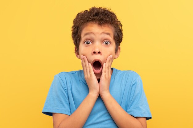 Shocked boy with hands on face open mouth on yellow background